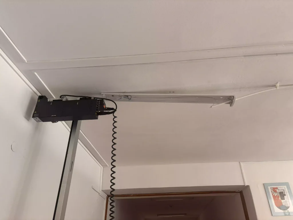 Głowica drukarki ściennej przejeżdżająca tuż pod sufitem po zdemontowaniu lampy na szkolnym korytarzu